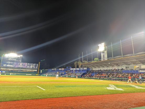 photo from ground level 3rd base of a baseball park with a pitcher on the mound and batter/catcher/umpire watching attentively