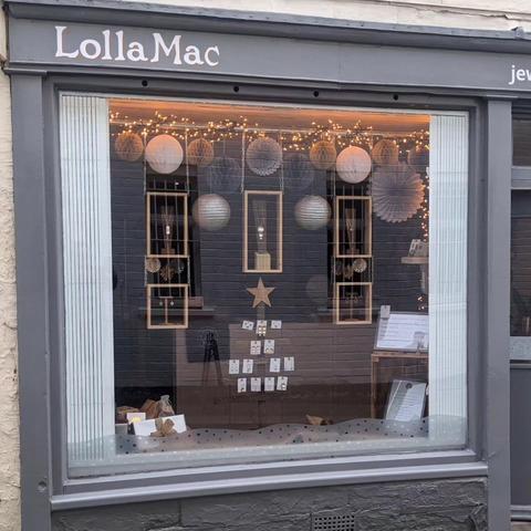 The LollaMac shop window decorated for winter, with white and silver paper balls hanging in the window, golden fairy lights, and an earring display in the shape of a Xmas tree with a star at the top.