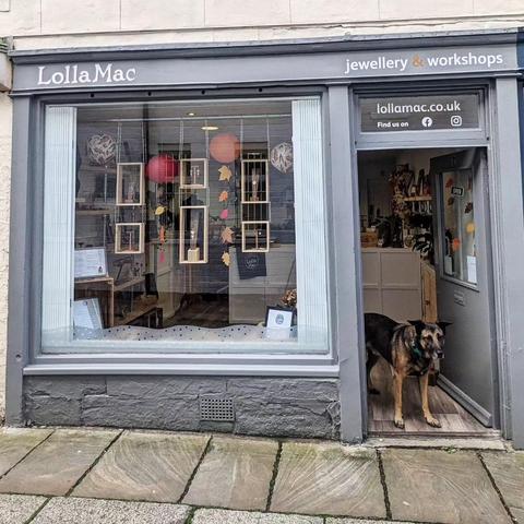 The LollaMac shop window decorated for autumn, with orangey paper balls and autumnal leaves. There is a familiar-looking dog standing in the doorway.