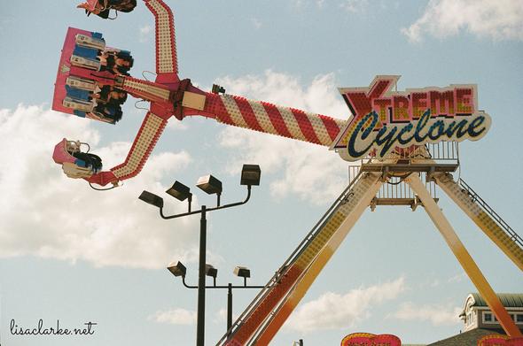 The "Xtreme Cyclone" amusement, caught frozen in time, as it swings its arm up in the air like a pendulum, while simultaneously spinning the passengers seated in its claw.