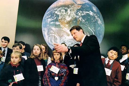 Al Gore with a group of children standing in front of a large photo of the Earth.