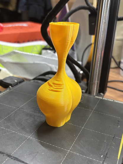 The same vase on the print bed a very thin neck some drooping from lack of supports and a seam running through it