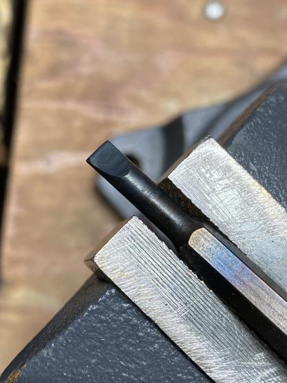 a repaired/reshaped formerly-broken screwdriver bit rehardened and blackened, held in a vise for final cooling after having been quenched in oil