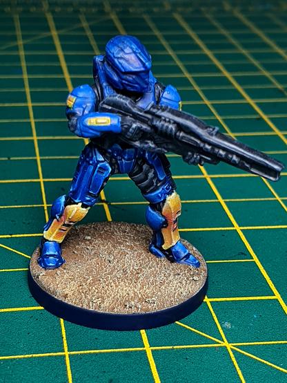 A photo showing a partly painted miniature. A halo Spartan in blue armour and yellow greaves.