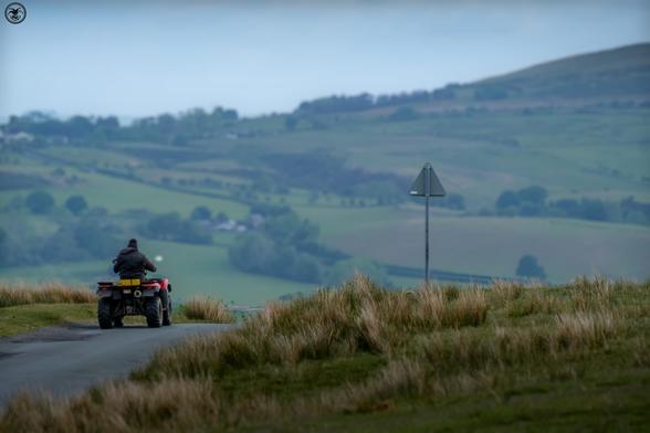 farmer on quad bike on moorland narrow road with views over countryside in background