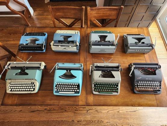 Two rows of four typewriters each lined up on opposite sides of a table.