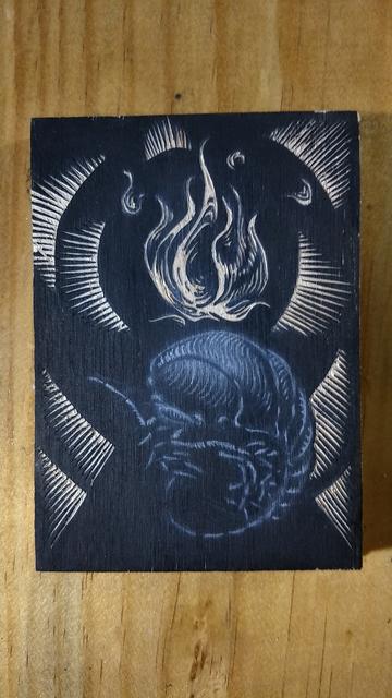 Fotografía de una imagen en el proceso de su grabado sobre un trozo de madera.

La imagen representada es de una flama flotante sobre una cochinilla en posición semi esférica.