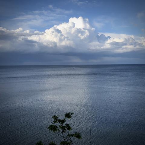 Wasser und dicke oben weiße, unten dunkle Wolken. Starke glänzende Spiegelung im Wasser.