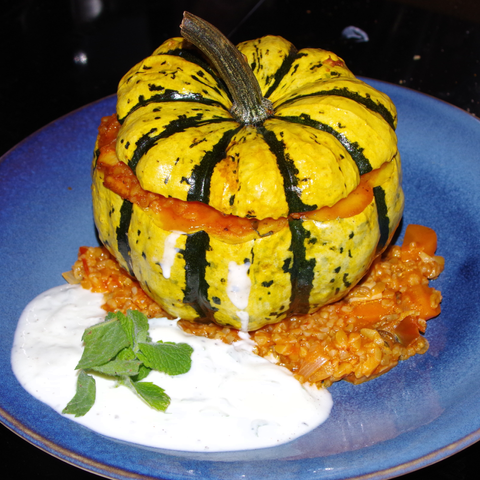 Gebackener gefüllter Kürbis auf blauem Teller mit Tomatenreis und angemachtem Joghurt.