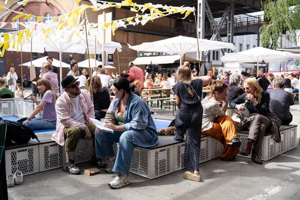 Foto von der republica 2024. Man sieht einen Innenhof mit Sonnenschirmen und Wimpeln. Verschiedene Personengruppen sitzen auf Kisten und Bierbänken und unterhalten sich.