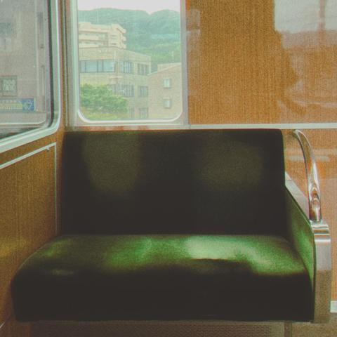 An empty green seat on a train stopped in front of a green mountain with tan buildings in front of the mountain.
