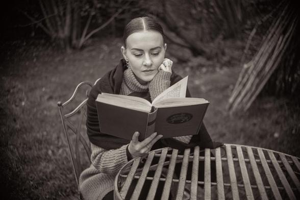 Frau, die an einem Gartentisch sitzt und in "Tristan und Isolde" liest