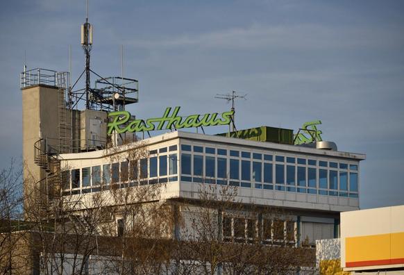 Oberer Teil eines Gebäudes mit rundum Fenstern. Auf dem Dach steht in grünen Buchstaben der Schriftzug Rasthaus. Links davon eine Wendeltreppe und ein kleiner Betonturm mit Antennen darauf.