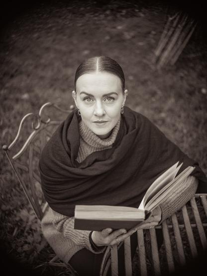 Frau, die im Garten an einem Tisch sitzt und in "Tristan und Isolde" liest