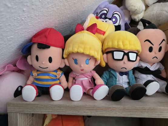 the mother 2/earthbound protagonists, unboxed, in my plushie shelf, along with some other, unrelated plushies (and a mr. saturn in his house)