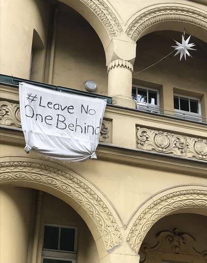 An opulent building facade with a white banner on which Leave no one behind is written
