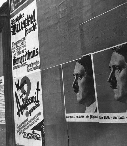Österreich, Wien: Stadtansichten; Eine Plakatwand im März 1938. Auf der dunklen Wand rechts zeri Plakate mit Hitler im Profil und der Aufschrift "Ein Volk - ein Reich- ein Führer". Links zwei Plakate, die Propagandveranstaltungen im konzerthaus anbringen sowie vom Volksblatt : "Warum bin ich Antisemit geworden?" Nachweis von wiki commons.