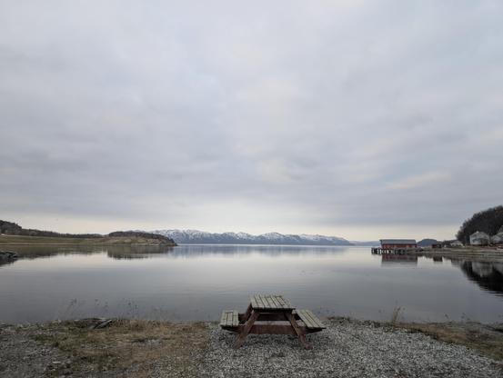 Picnic table near the sea, with mountains in the background and a grey sky.