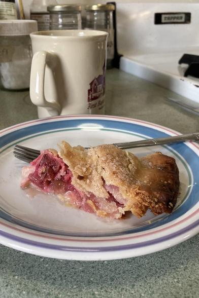 A slice of homemade, rhubarb pie.  The filling has a pleasant rosy color. The crust is flaky and a little bit toasty.