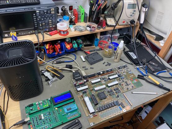 Amiga 500 Revision 5 Board on my workbench with all kinds of tools, chips and the retro chip tester scattered around it. Many chips on the board were socketed and the lower row of RAM is desoldered in the picture for testing.