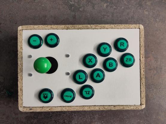 A top-down view of an arcade controller made of compressed wood with green buttons