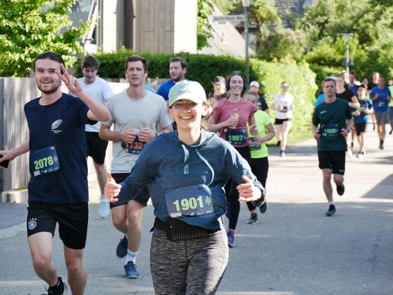 Another group of runners is jogging along the same street, some waving or smiling at the camera. The atmosphere is motivated and friendly.