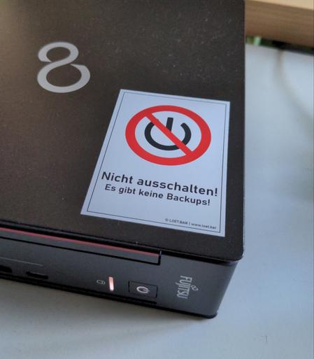 Aufkleber auf einer schwarzen Workstation: 'Nicht ausschalten! Es gibt keine Backups!'