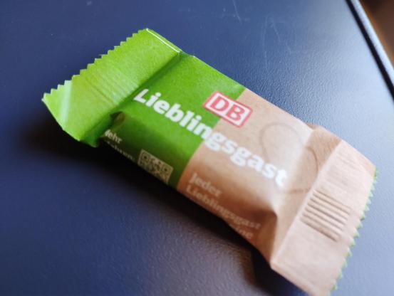 A green and brown paper packet on containing chocolate. The packet is on a blue background and below the DB logo is the word Lieblingsgast.