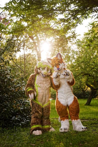 A portrait of Fullsuiter Gustl and Fox Flummox against the evening sunlight in a park with lots of trees in the background