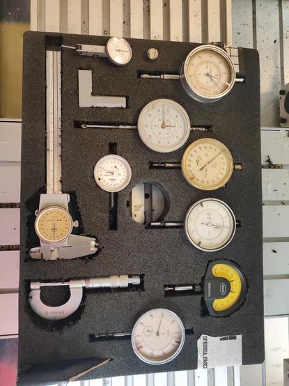 A piece of foam with pockets of several measuring tools in it. Among them: Dial Calipers, a small machinists square, a micrometer, a small straight edge, a dti (mahr puppitast) and several (7) indicators of different resolution and ranges.