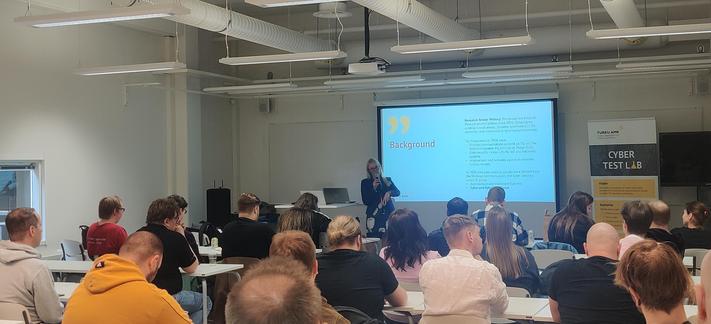 A classroom full of people with Päivi speaking in front of the room