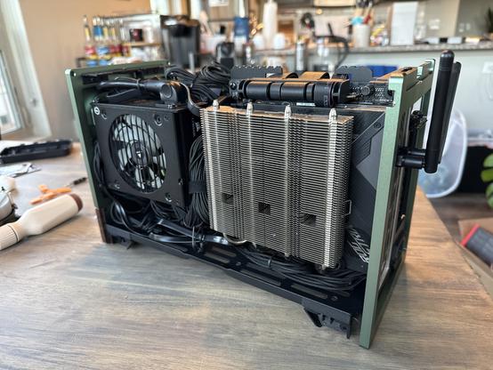 Side profile of my mini ITX PC with the side panel off. The power supply is mounted on the left, and the giant, silver CPU cooler is covering the motherboard on the right. The power supply cables are routed in the minimal empty space.