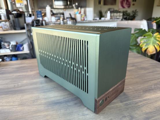 An angled photo of my PC with all of the side panels on. It is a metallic, jade green with slits along the side of ventilation. The front is solid jade, with a walnut wood panel on the bottom with the power button and front panel IO.