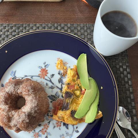 A blue and gold edged plate with a sugared mini-bunt and a slice of frittata topped with avocado slices. and a steaming cup of coffee in the background.