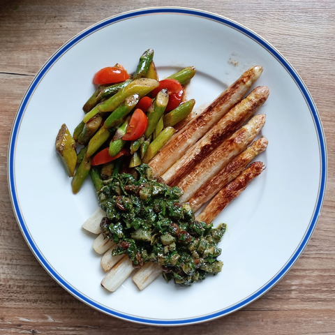 Gebratener weißer Spargel mit einer grünen Sauce, in der man die Cornichons sieht. 
Daneben ein Salat auf grünem Spargel und Tomaten