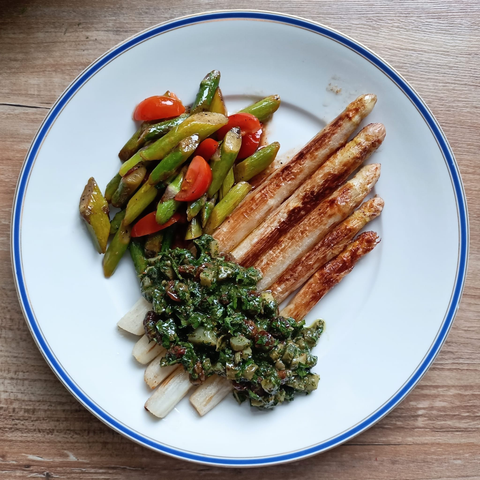 Gebratener weißer Spargel mit einer grünen Sauce, in der man die Cornichons sieht. 
Daneben ein Salat auf grünem Spargel und Tomaten