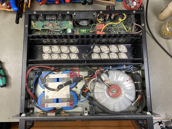 The innards of a beefy PA power amp (HH Electronic MX 900) on my workbench with a huge toroidal transformer, some other circuitry and 16 TO-3 transistors in the power amp section visible.