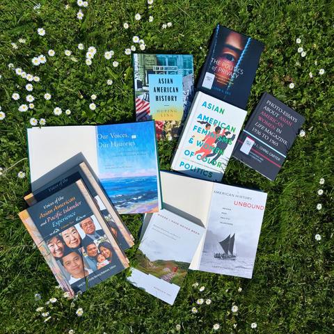 A selection of books on Asian American & Pacific Islander American topics on a meadow with green grass and daisies