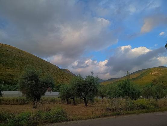 Strada asfaltata in campagna, con montagne all'orizzonte e cielo nuvoloso.
