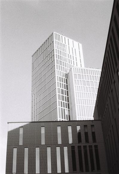Black-and-white photo of several very rectangular hotel buildings in different heights, looking like assorted building blocks towering up against the grey sky. They all have plain façades covered in rectangular windows of wildly varying widths. It's all very geometric.