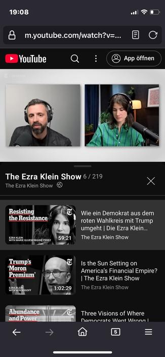 The image shows a mobile screen displaying a YouTube video titled "The Ezra Klein Show." It features two hosts, one male with a beard and headphones, and one female with long hair, also wearing headphones. Below the video, there are thumbnails, the first is the AI generated German translation.