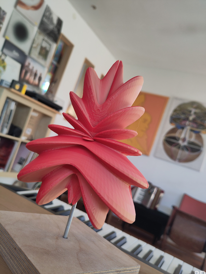 Eine #Kleinplastik, welche an eine symmetrische Koralle erinnert, aus rotem Kunststoff auf einem Ständer.
