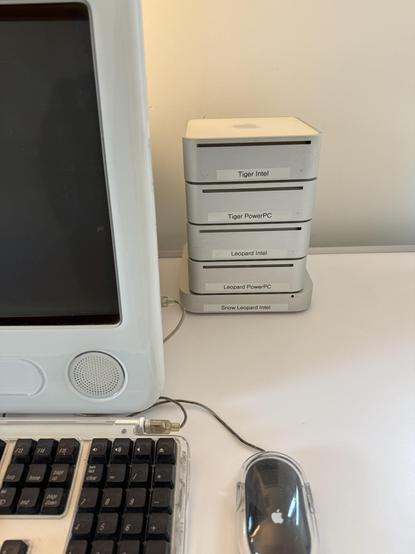 A stack of five Mac Minis next to an eMac computer. The Minis have labels identifying which operating system version and CPU type is running on them.
