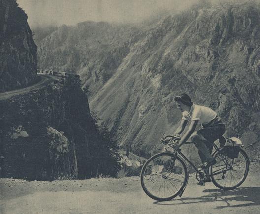 une cycliste sur une route vertigineuse, des montagnes au loin