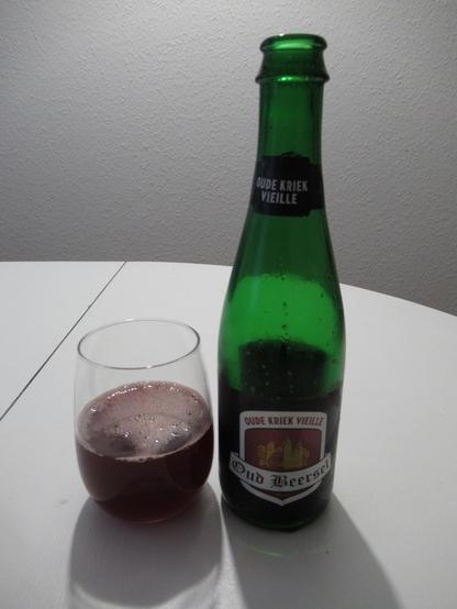 A glass of cherry-red beer next to a bottle labeled "Oud Beersel Oude Kriek Vielle"