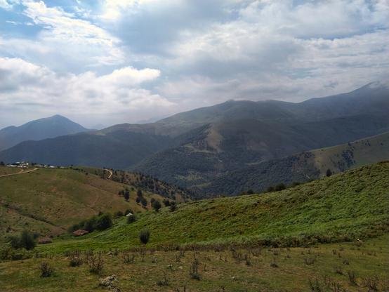 تصویری از کوهستان سرسبز روستای اسب ونی در مرتفع‌ترین منطقه جاده اسالم به خلخال. شامل کوه های پوشیده از سبزه و آسمان نیمه ابری.