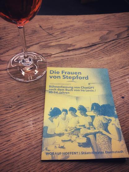 Foto:  Programmheft Staatstheater Darmstadt "die Frauen von Stepford" mit Stil von Weinglas auf Holz.