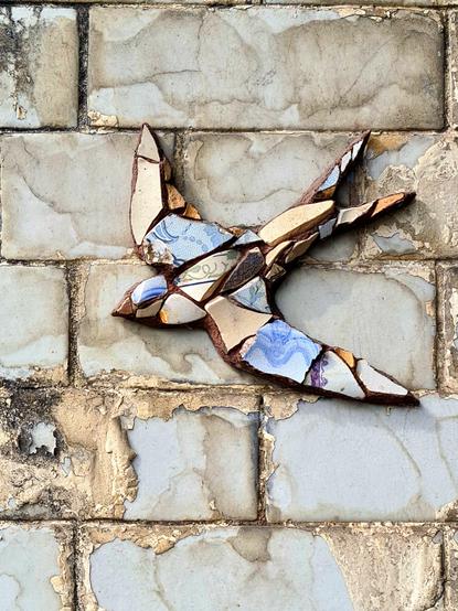 A swallow made from fragments of pottery on a Victorian wall made from glazed bricks.