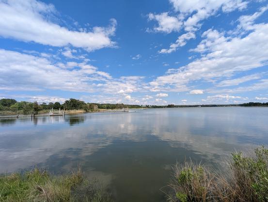 Photo of a calm afternoon on Harris Creek, sky is deep blue and decorated with puffy white clouds. Marsh is a riot of new green growth. Creek water is rippled and reflects sky and clouds.