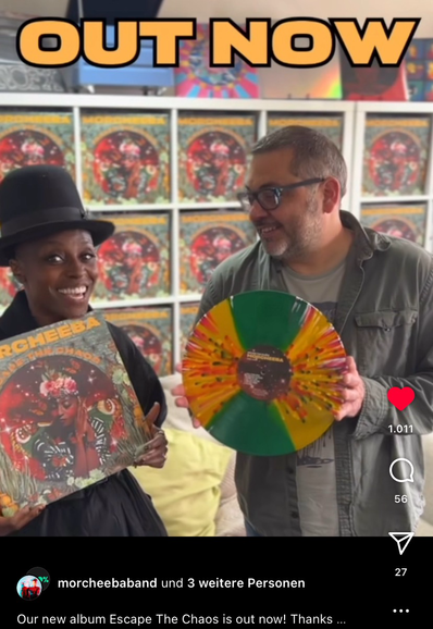 Screenshot of a promo with Skye Edwards and Ross Godfrey, both holding the vinyl limited edition of „Escape the Chaos“ in their hands, Skye with a wide smile, Ross looking at her.